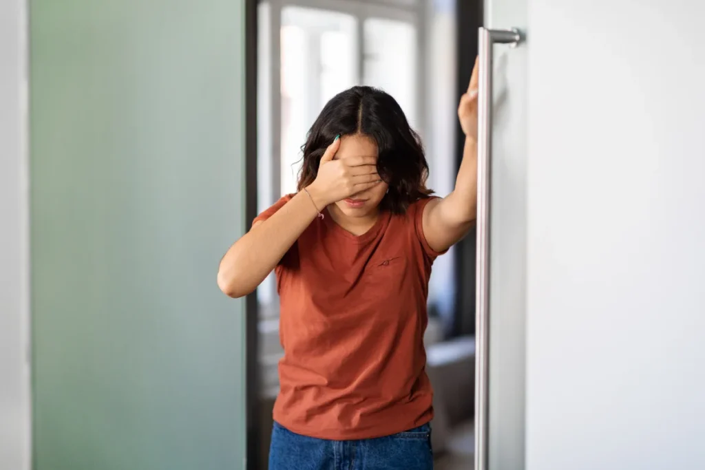 A woman leaning on a doorway with one hand and her other hand on her head from being dizzy