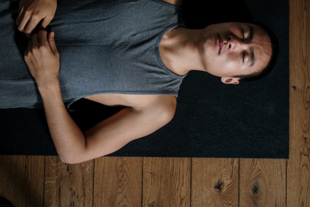 Man lying supine on a mat with eyes closed, hands resting on his stomach