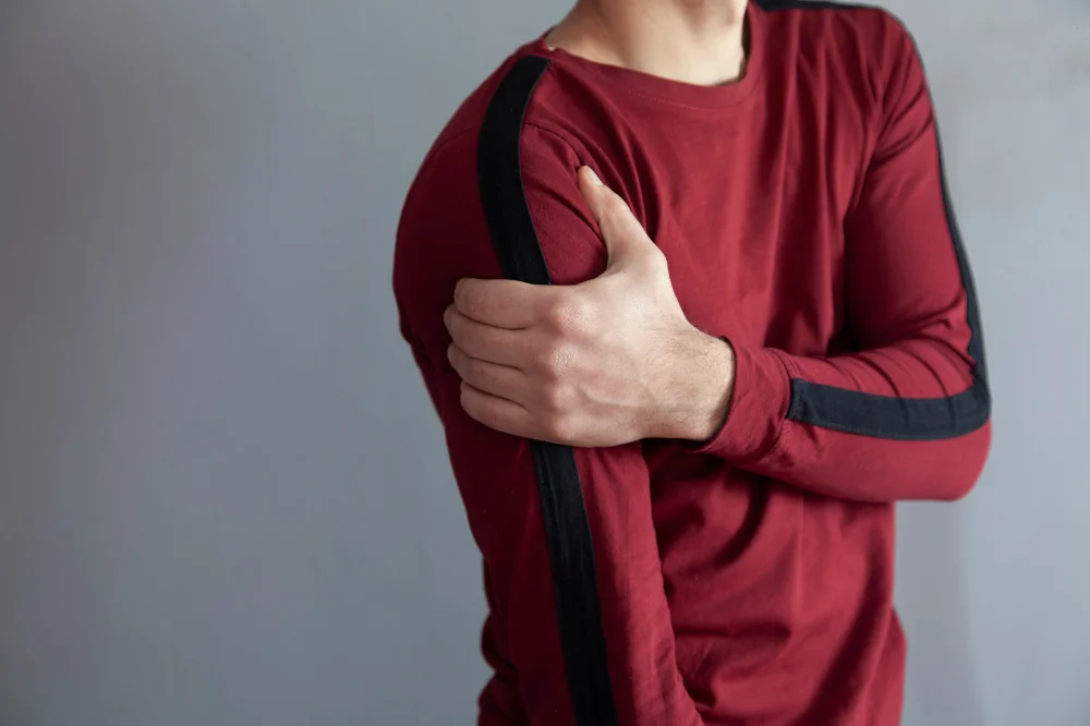 A view of a persons torso, they are gripping their shoulder with the opposite arm like in a shoulder subluxation