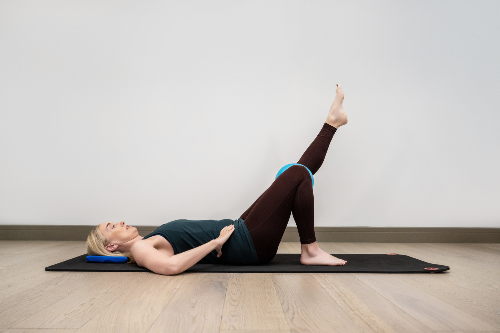 Jeannie lays on her back on a mat. One knee is bent and one is extended into the air doing a knee exercise for hypermobility.