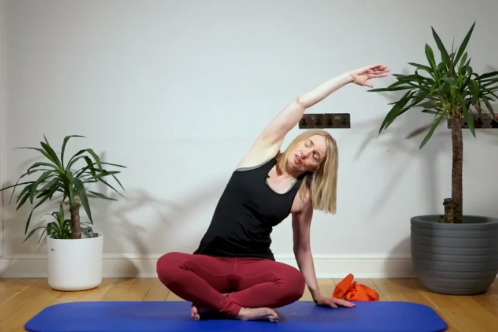 Jeannie sitting on blocks on a pilates mat doing a side bend with an arm in the air 