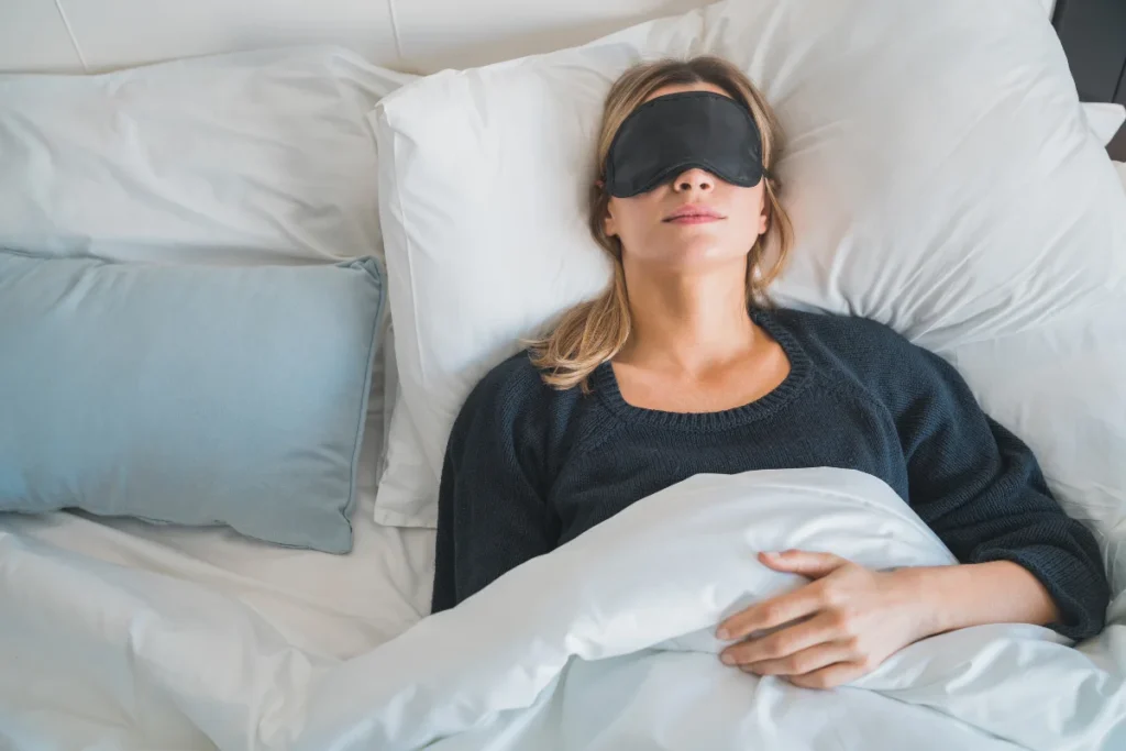 woman sleeping on her back with her head on a pillow and a sleeping mask covering her eyes 