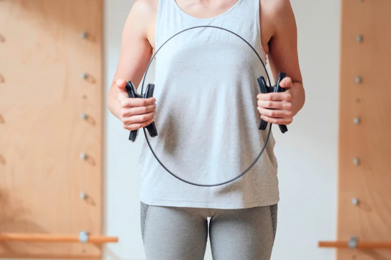 a woman holding a pilates ring in front of her torso. Her head and and lower legs are not visible. 
