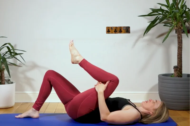 Jeannie stretching her hamstring laying on a pilates mat with one leg pulled towards her