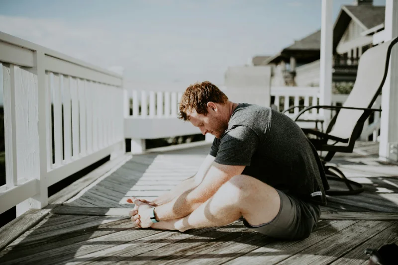 man sits and does butterfly leg stretch on a porch outside 