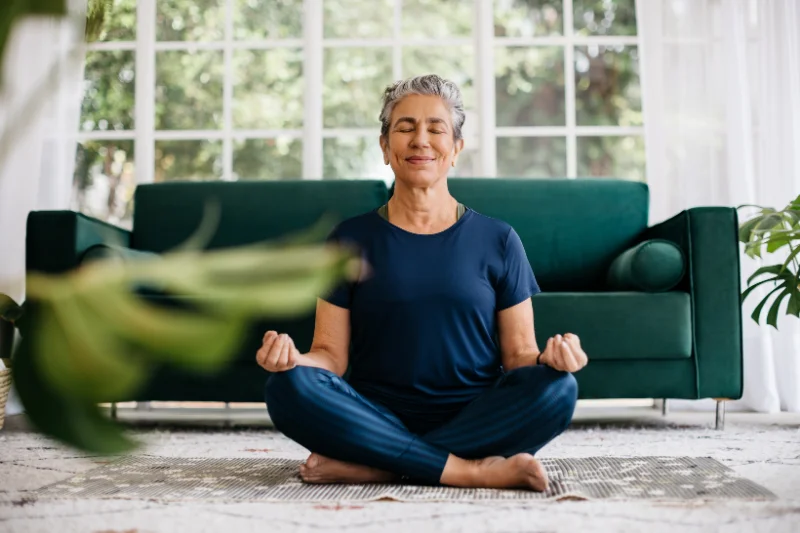 Older woman meditating at home, illustrating mindfulness for chronic pain and hypermobility