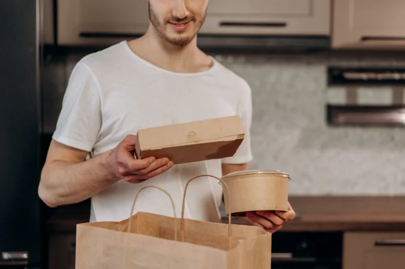 A man pulls cardboard take out containers out of a paper bag