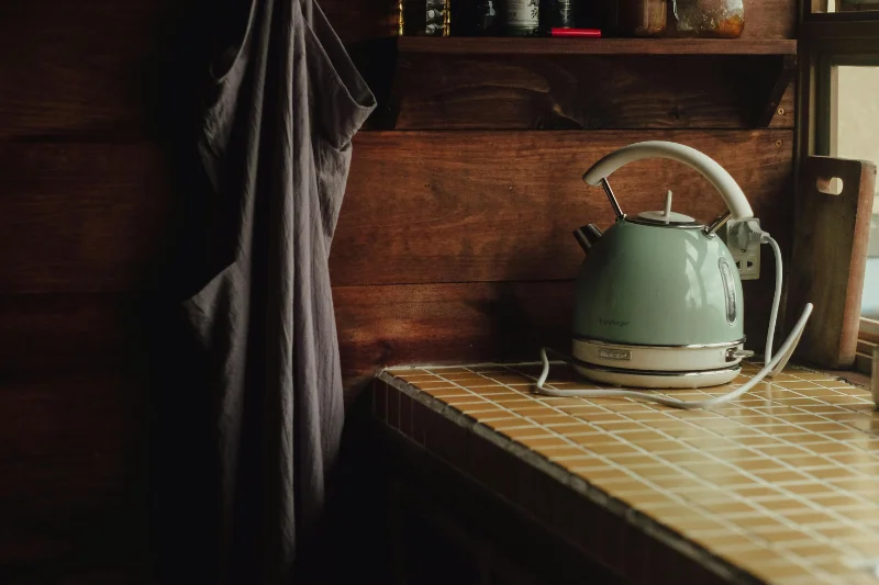 a tea kettle on a counter with mugs on a shelf above it