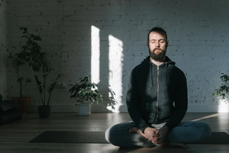A man sits crossed legged on a yoga mat with his eyes closed
