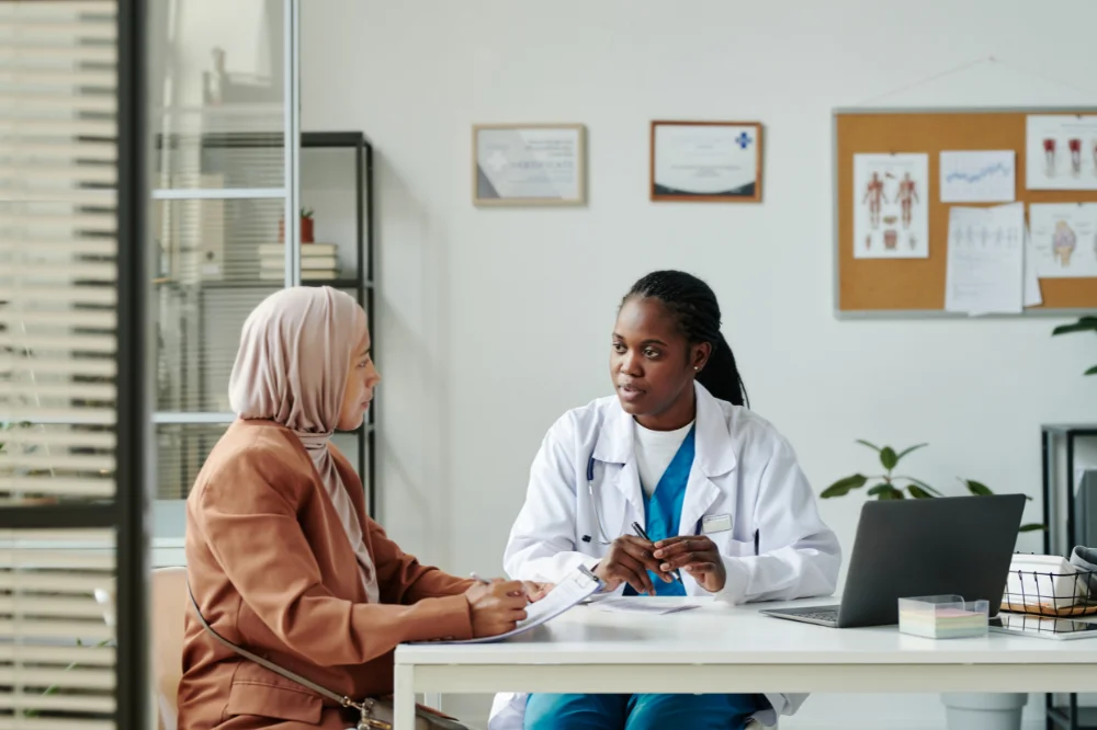 Two women sit together at a desk in conversation, one a healthcare professional reviewing information with her patient.